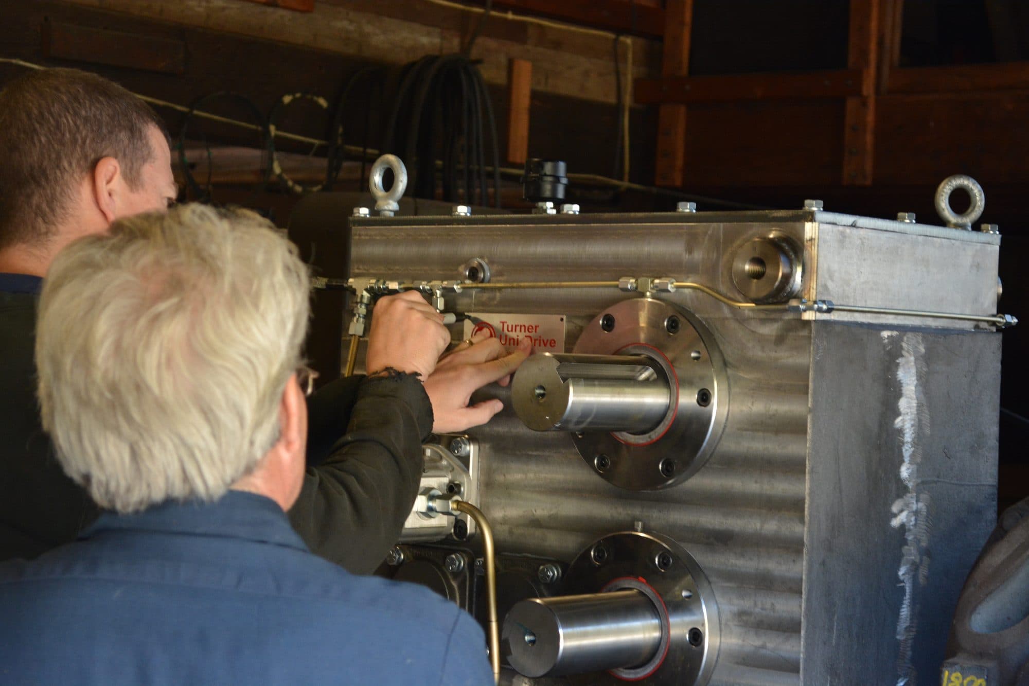 Two machinists assembling a large industrial gearbox on a manufacturing shop floor
